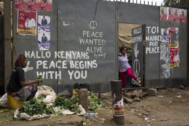 A Kenyan woman walks through a gate covered with graffiti calling for peace in Nairobi's Kibera slum