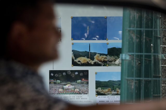 A man drives his car past a display board showing photos of ballistic missile launches in North Korea outside the North Korean embassy in Beijing