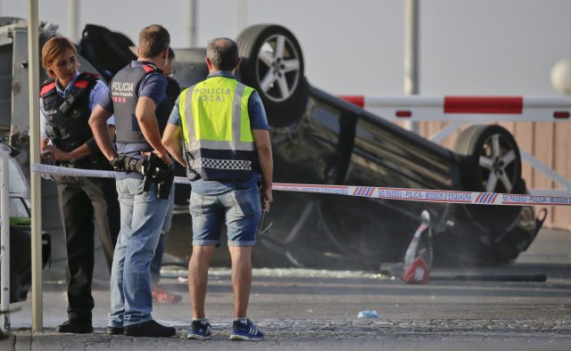 Police officers stand near an overturned car at the spot where terrorists were intercepted by police in Cambrils, Spain