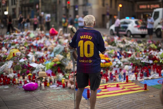 A man stands next to flags, flowers, messages and candles to the victims on Barcelona's historic Las Ramblas promenade 