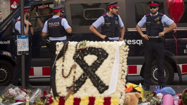 Police officers stand guard next to flags, flowers, messages and candles to the victims on Barcelona's historic Las Ramblas promenade