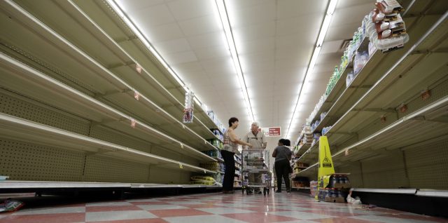 Shoppers pass empty shelves along the bottled water aisle in a Houston grocery store
