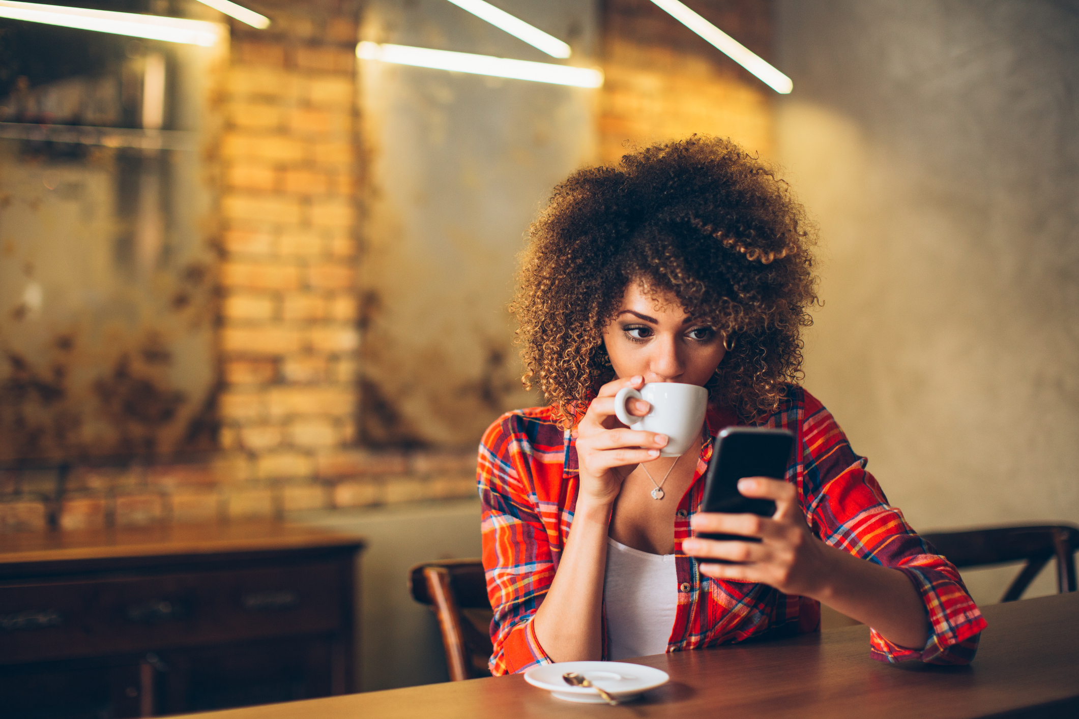 Young woman at cafe drinking coffee and using mobile phone (Thinkstock/PA)