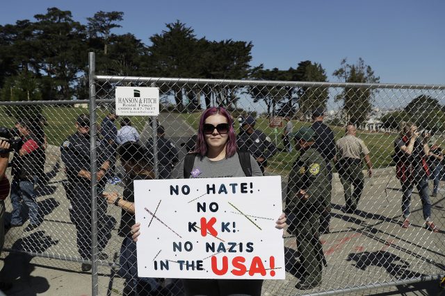 Andrea Smith holds up a sign in front of a fence blocking an entrance to Alamo Square Park in San Francisco