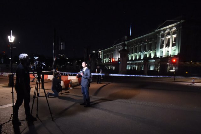 A reporter speaks to camera beside a police cordon outside Buckingham Palace 