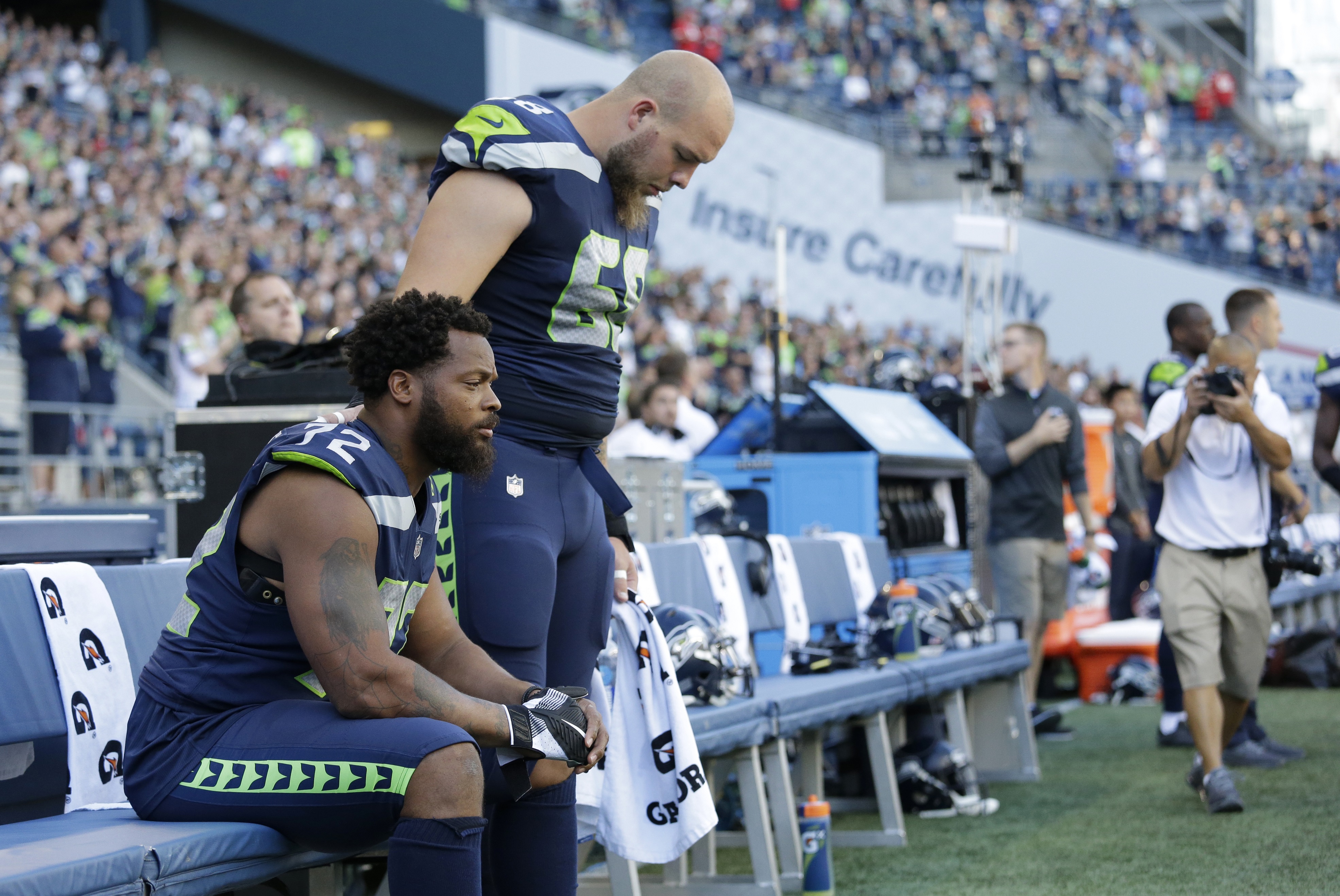 Seattle Seahawks defensive end Michael Bennett, left, sits during the singing of the national anthem as center Justin Britt, right, stands next to him