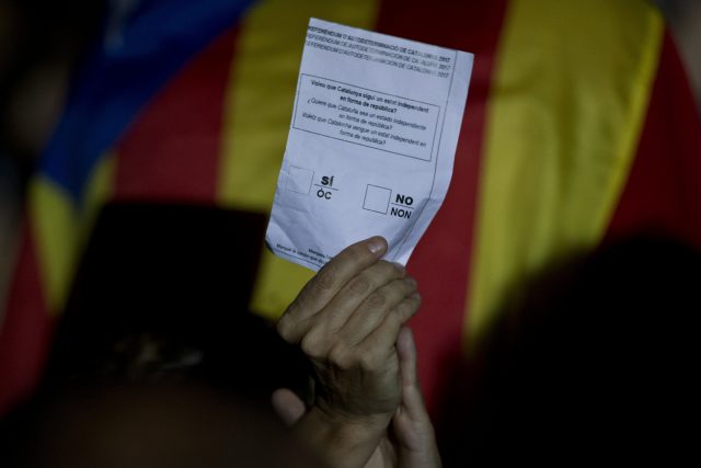 A woman holds an unofficial ballot paper next to an Estelada or Independence flag (Emilio Morenatti/AP)