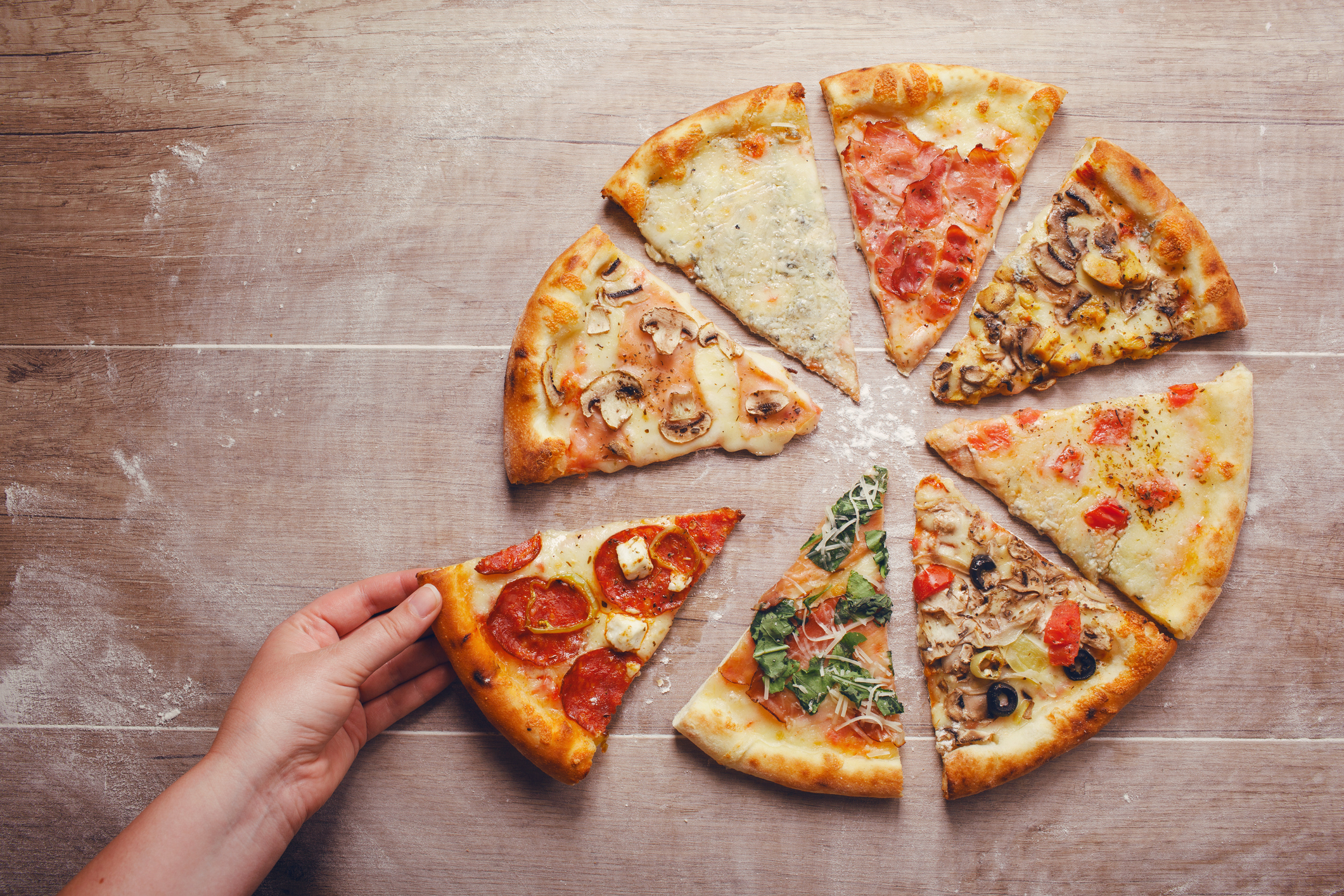 Hand taking slice of pizza with different toppings on a wooden background (Thinkstock/PA)
