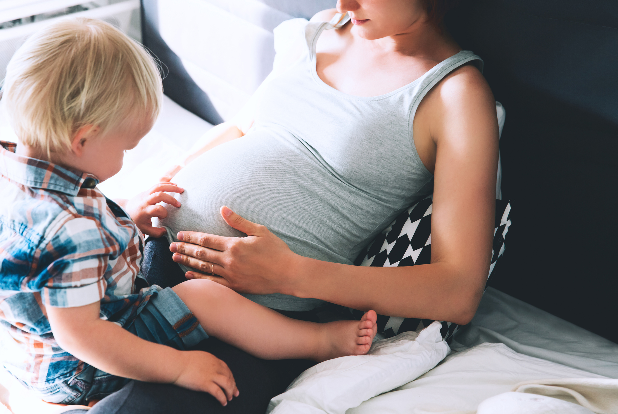 A little boy sits on his pregnant mum's lap, touching her tummy (Thinkstock/PA) 