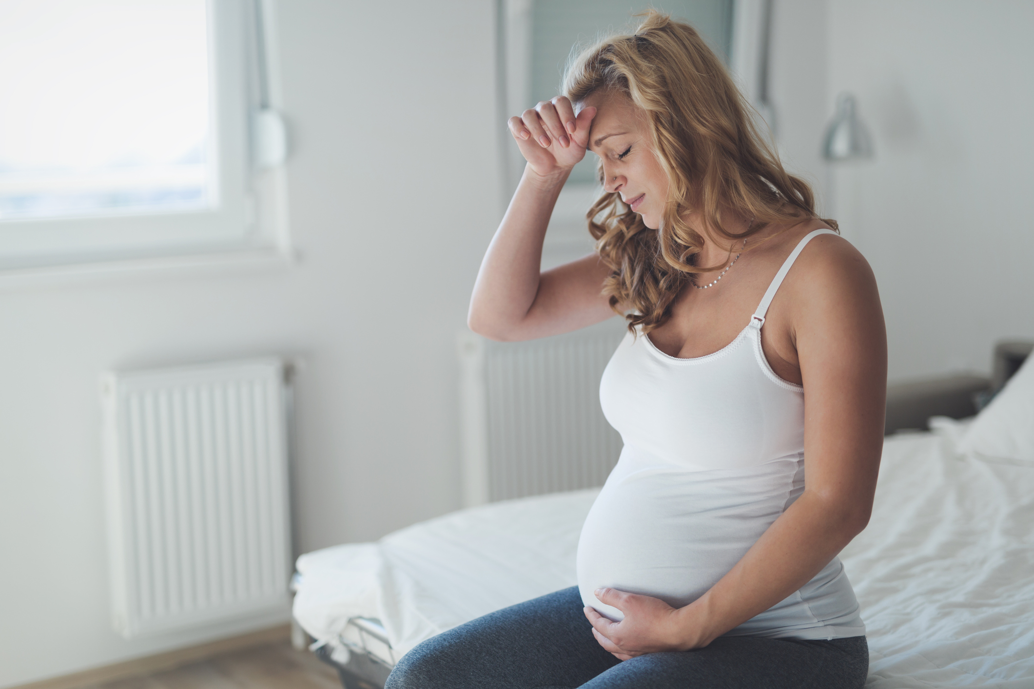 A pregnant woman looking worried, sitting on her bed (Thinkstock/PA)