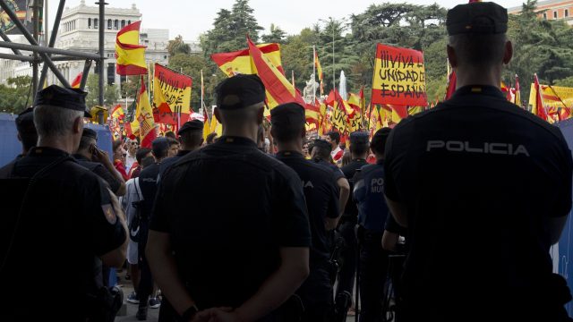 Police block the entrance of the city hall as protesters wave Spanish national flags in the central Cibeles square in Madrid