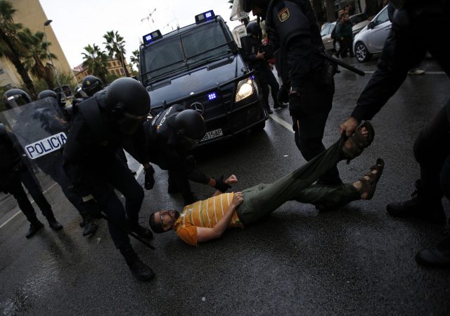 Spanish National Police officers drags a man trying to block a police van