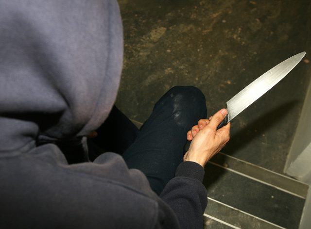 A general view of a man in a hoodie holding a knife
