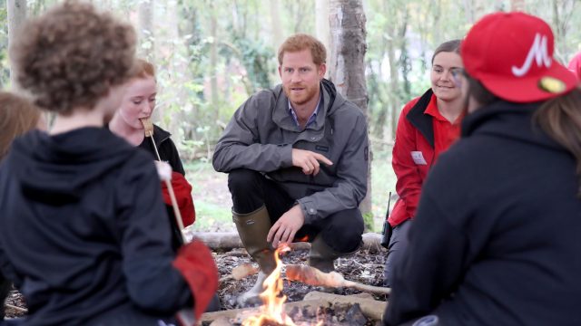 Prince Harry speaks to members of the group over a campfire