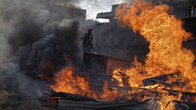 An opposition supporter pushes a wooden cabinet, looted from the property of a man of the Kikuyu tribe that they broke into, onto a burning barricade