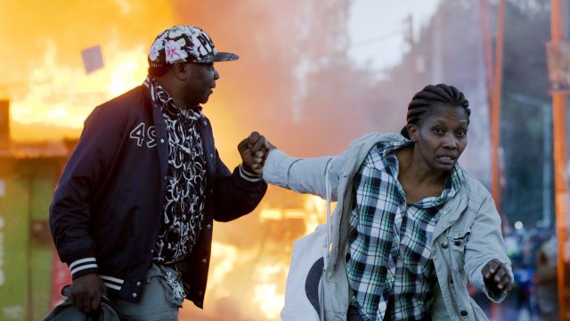 A couple run past burning shops during clashes in Nairobi