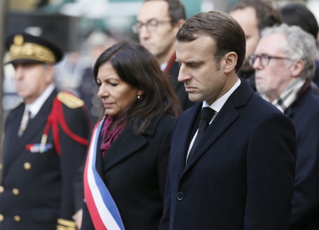 Emmanuel Macron and Paris mayor Anne Hidalgo stand in silence in front of the Comptoir Voltaire bar (Etienne Laurent, Pool via AP)