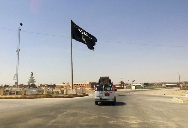 A motorist passes by a flag of the Islamic State group in central Rawah