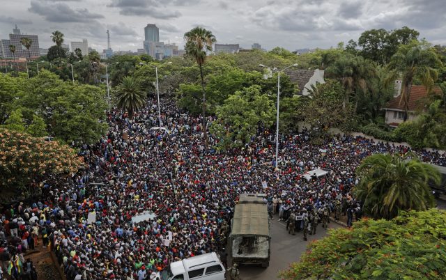 A crowd of thousands of protesters demanding President Robert Mugabe stands down gather behind an army cordon on the road leading to State House in Harare