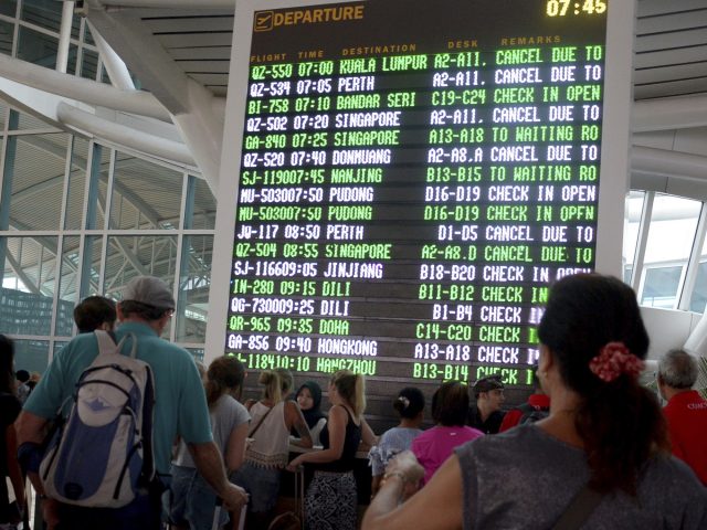 Passengers read flight information at Ngurah Rai International Airport in Bali