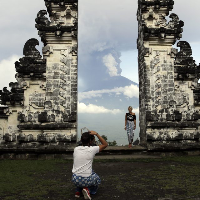 A tourist poses for a photo with Mount Agung in the background