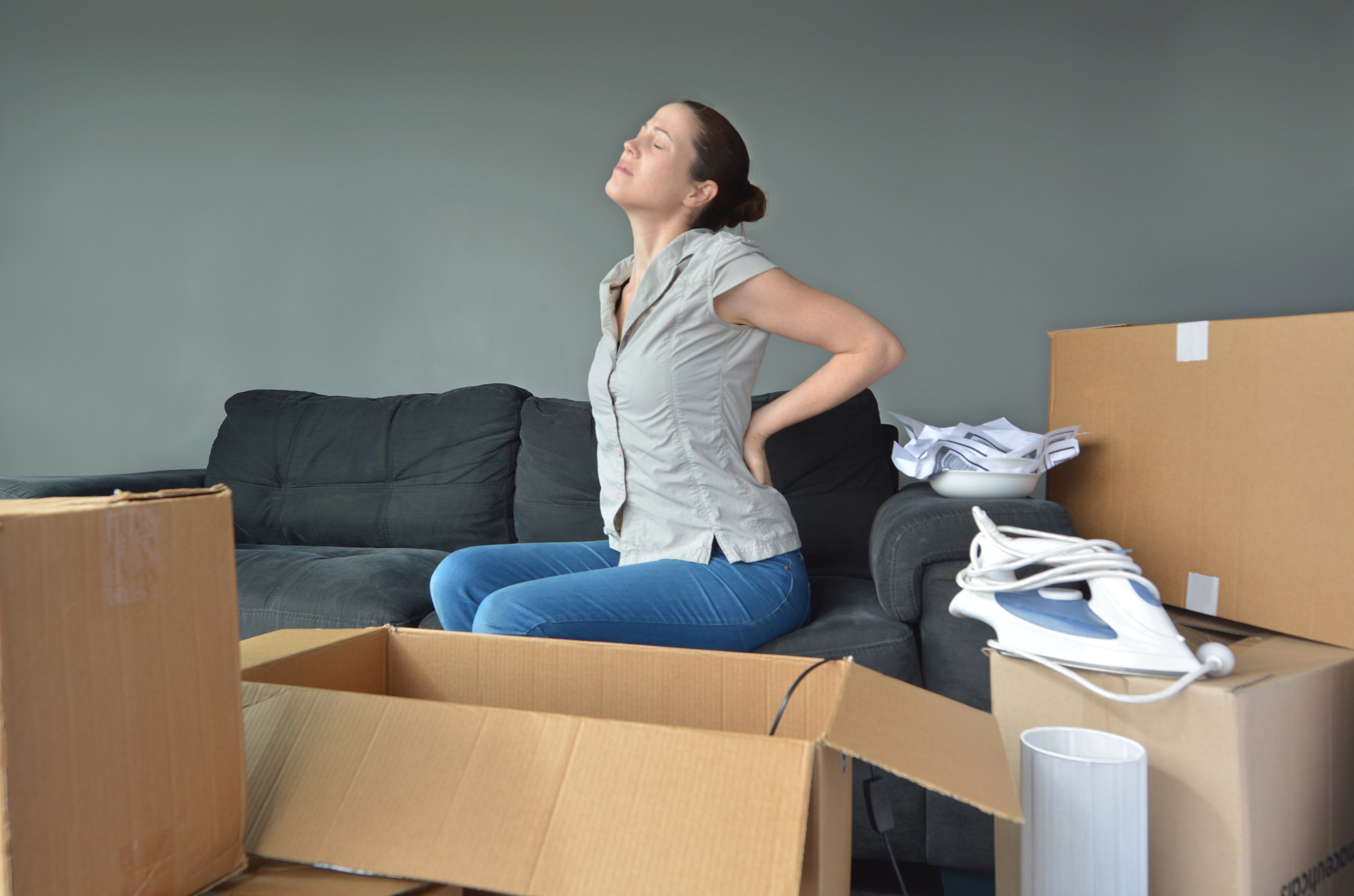 Woman holding her back in pain while surrounded by boxes (Thinkstock/PA)