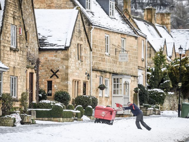 A postman pushes his trolley over snow on the High Street in Broadway, Worcestershire (PA)