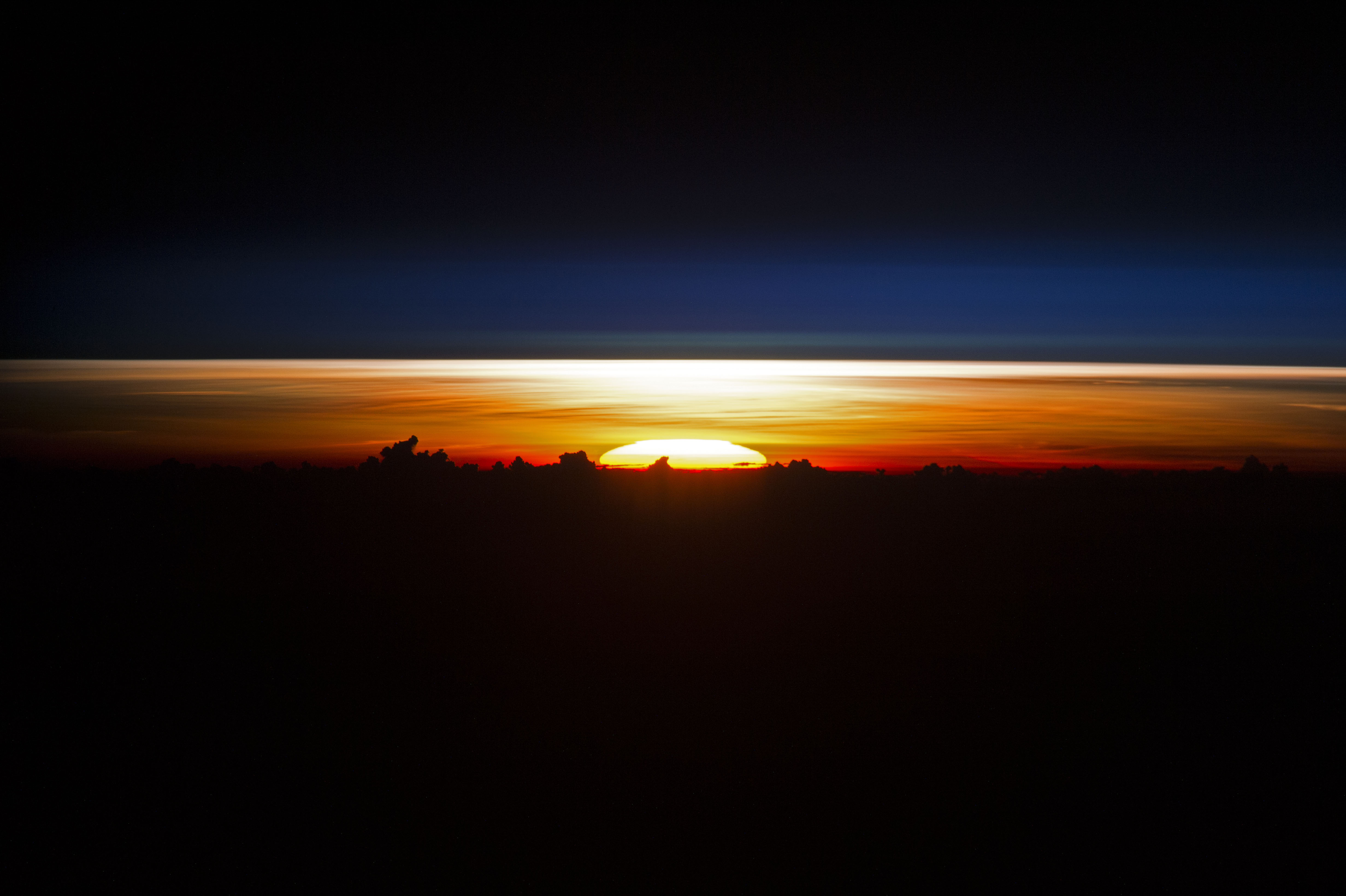  partial disc of the sun just as it began to rise, creating a sheet of light across the horizon. Silhouetted clouds give the sense of a jumbled mountain range. (Nasa)