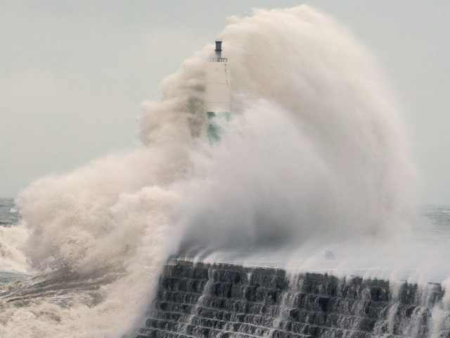 Waves crash over the stone jetty wall in Aberystwyth