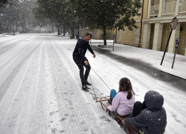 Ramon Martinez takes advantage of little car traffic to pull his children Amy and Anthony on a sleigh down Bull Street toward Monterey Square, in Savannah (Steve Bisson/Savannah Morning News via AP)
