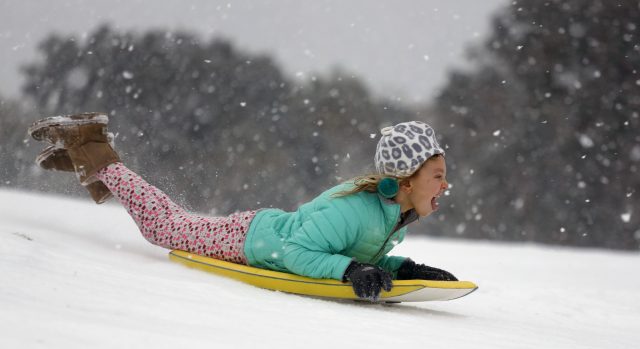 Finley Bork, seven, uses a boogie board, typically used on the beach, for sledding down a hill on a golf course at the Isle of Palms, South Carolina (Mic Smith/AP)