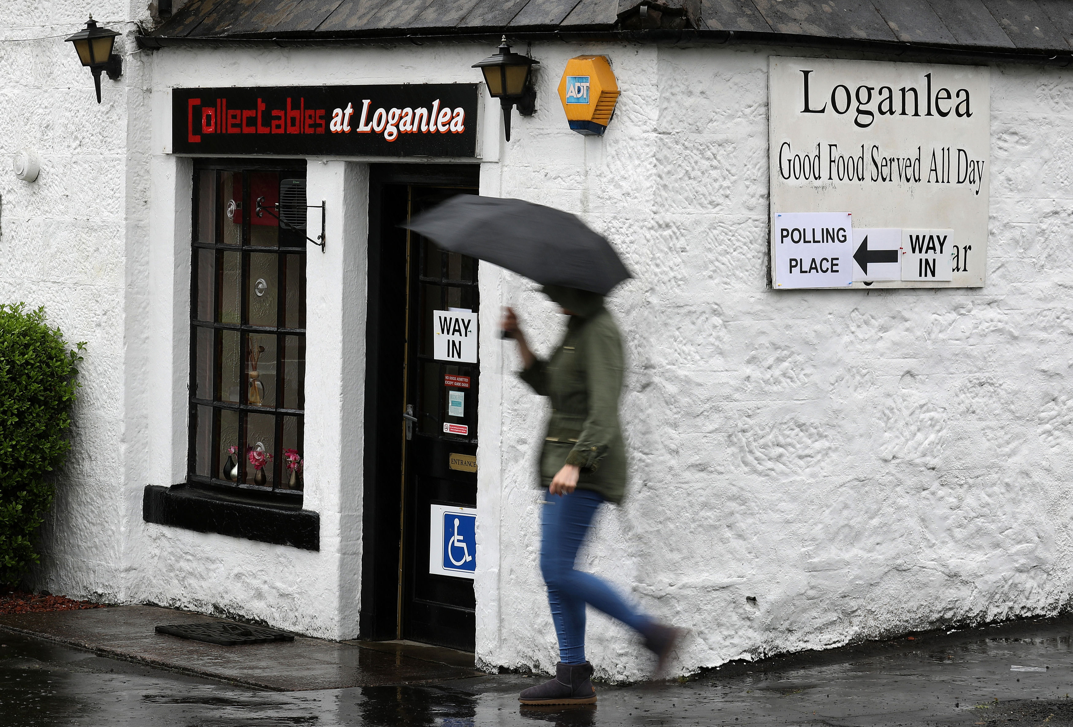 A man with an umbrella walks past a polling centre sign