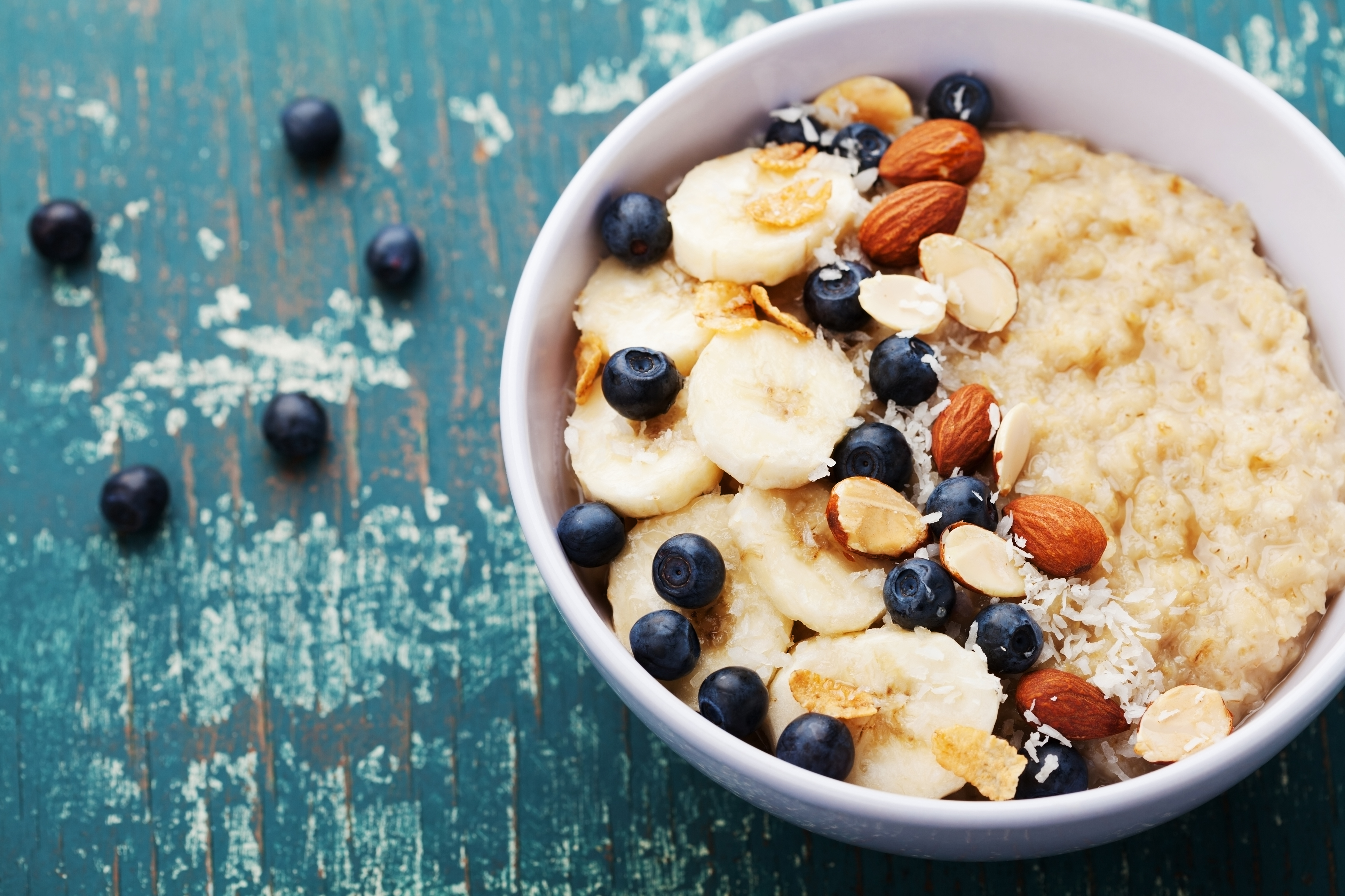 Bowl of homemade oatmeal porridge with banana, blueberries, almonds, coconut and caramel sauce on teal rustic table from above, hot and healthy food for Breakfast