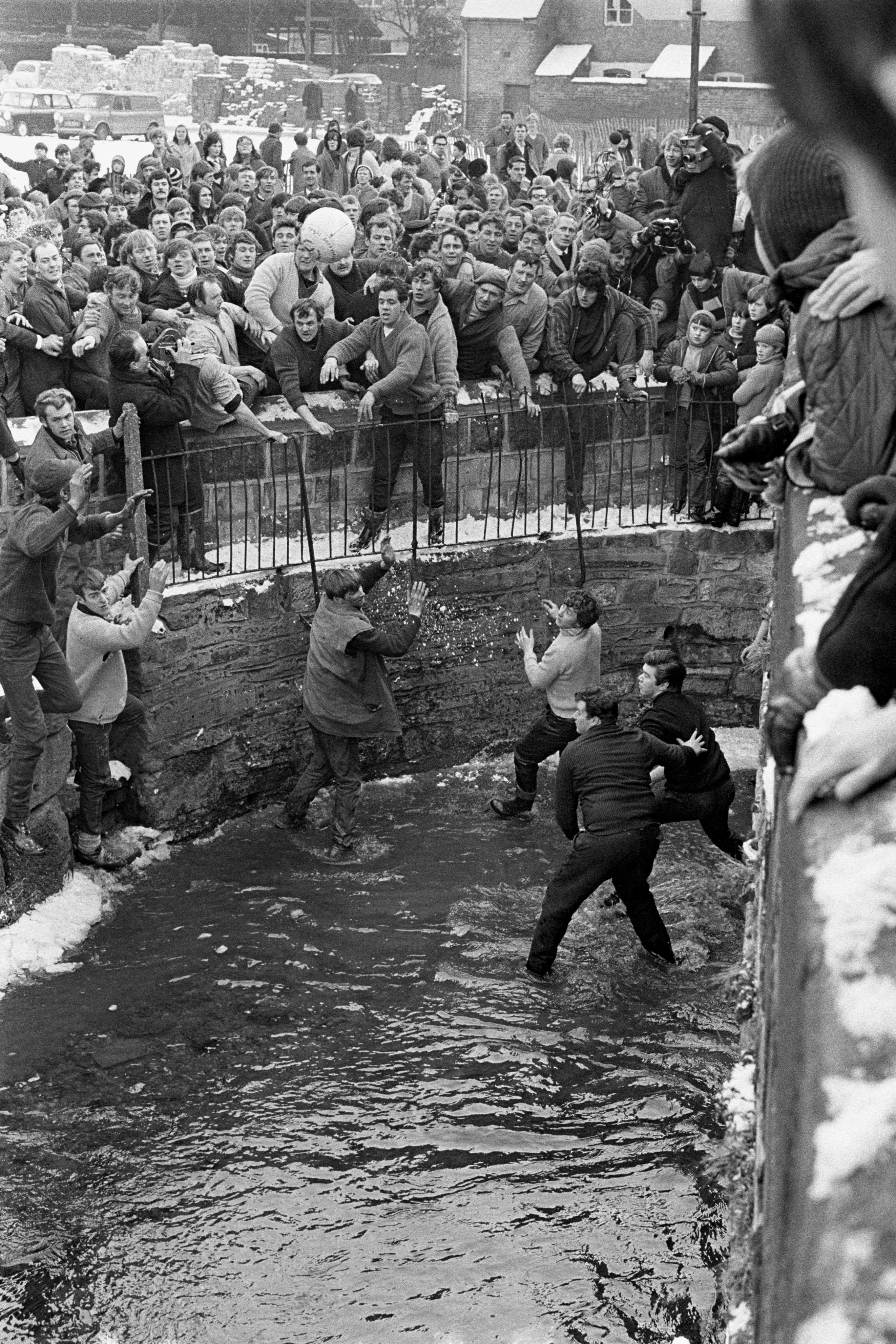 Black and white photo of men scrabbling river, and ball being thrown into it