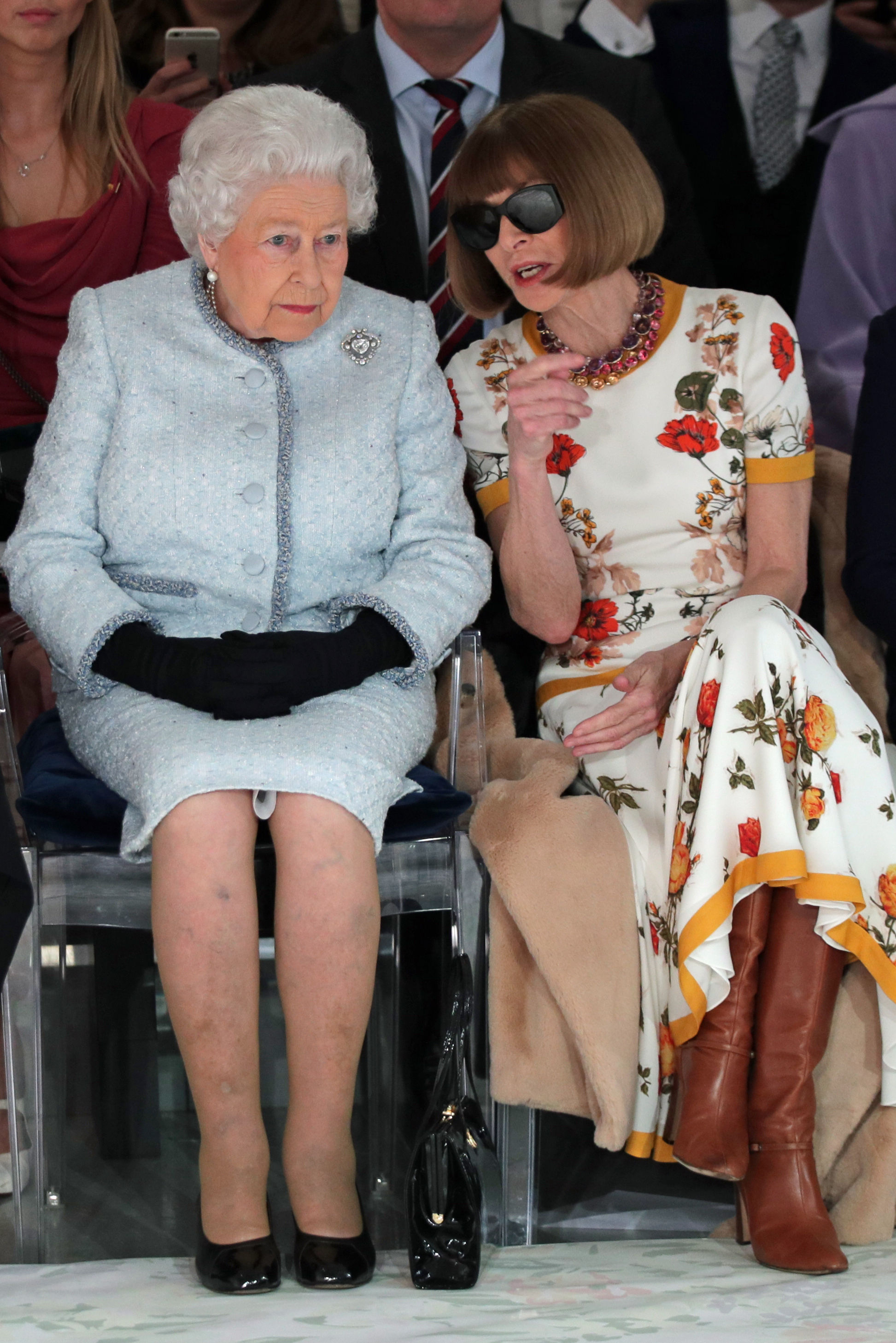The Queen sits next to Anna Wintour, who is speaking