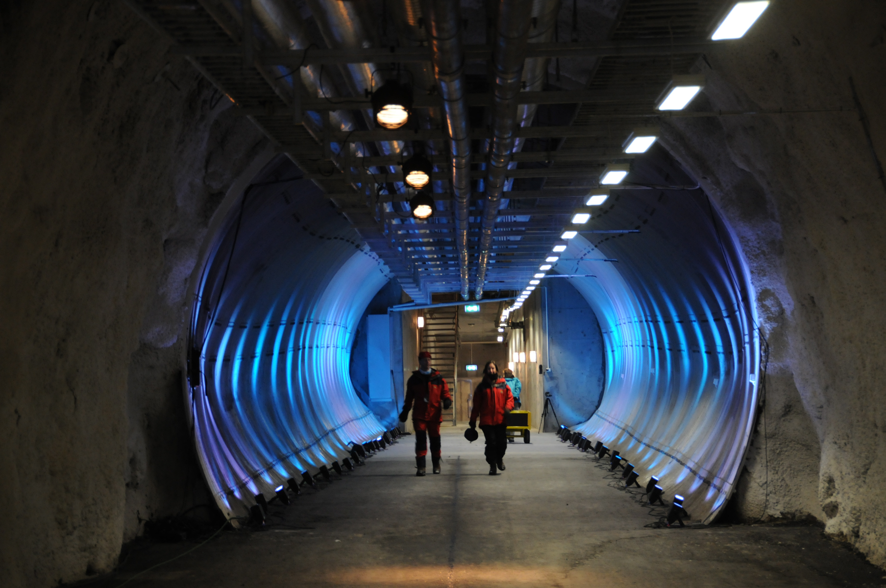 Two people walk through a dimly lit tunnel built into the side of a mountain