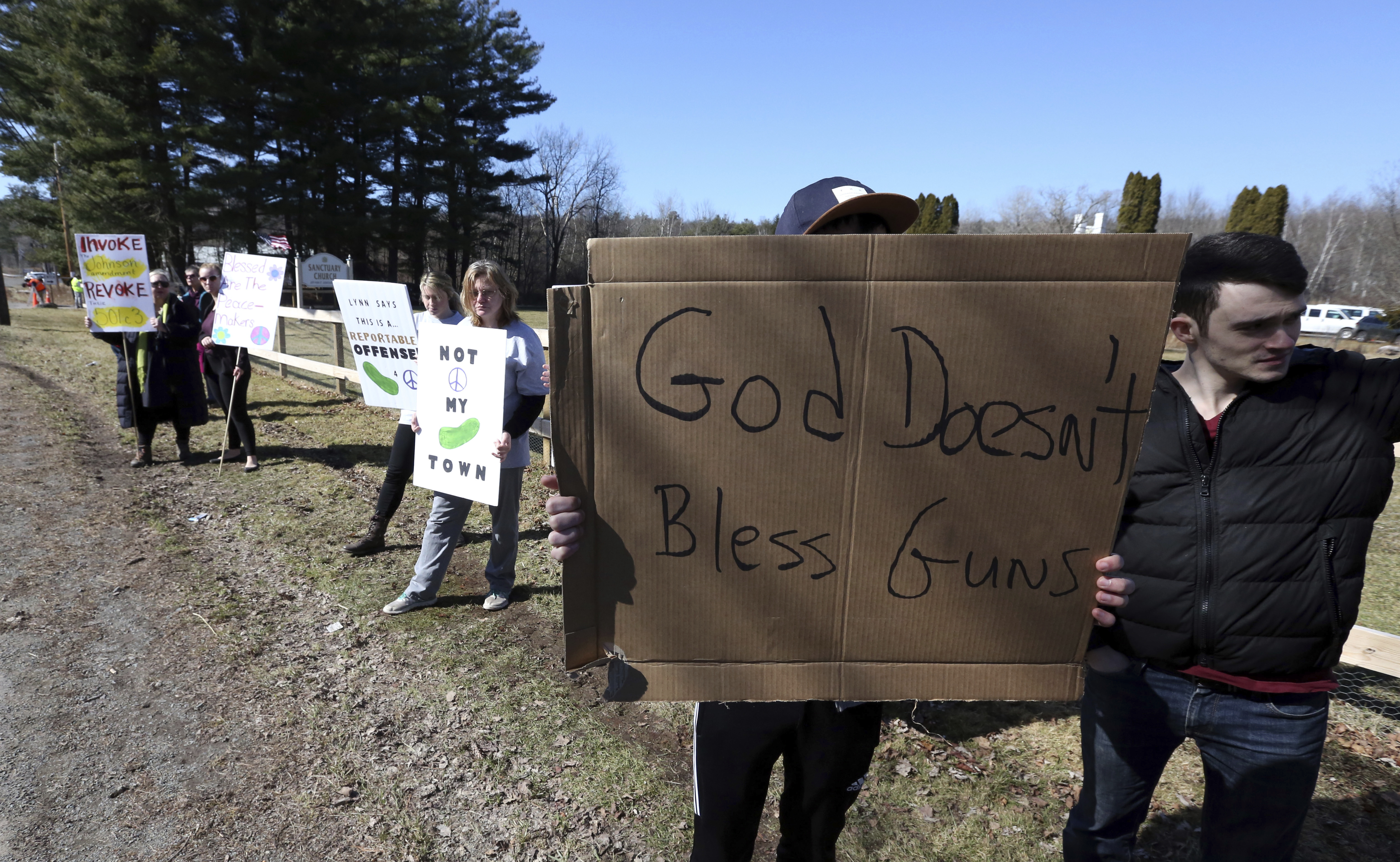 A protester outside the church with a sign saying 'God doesn't bless guns'