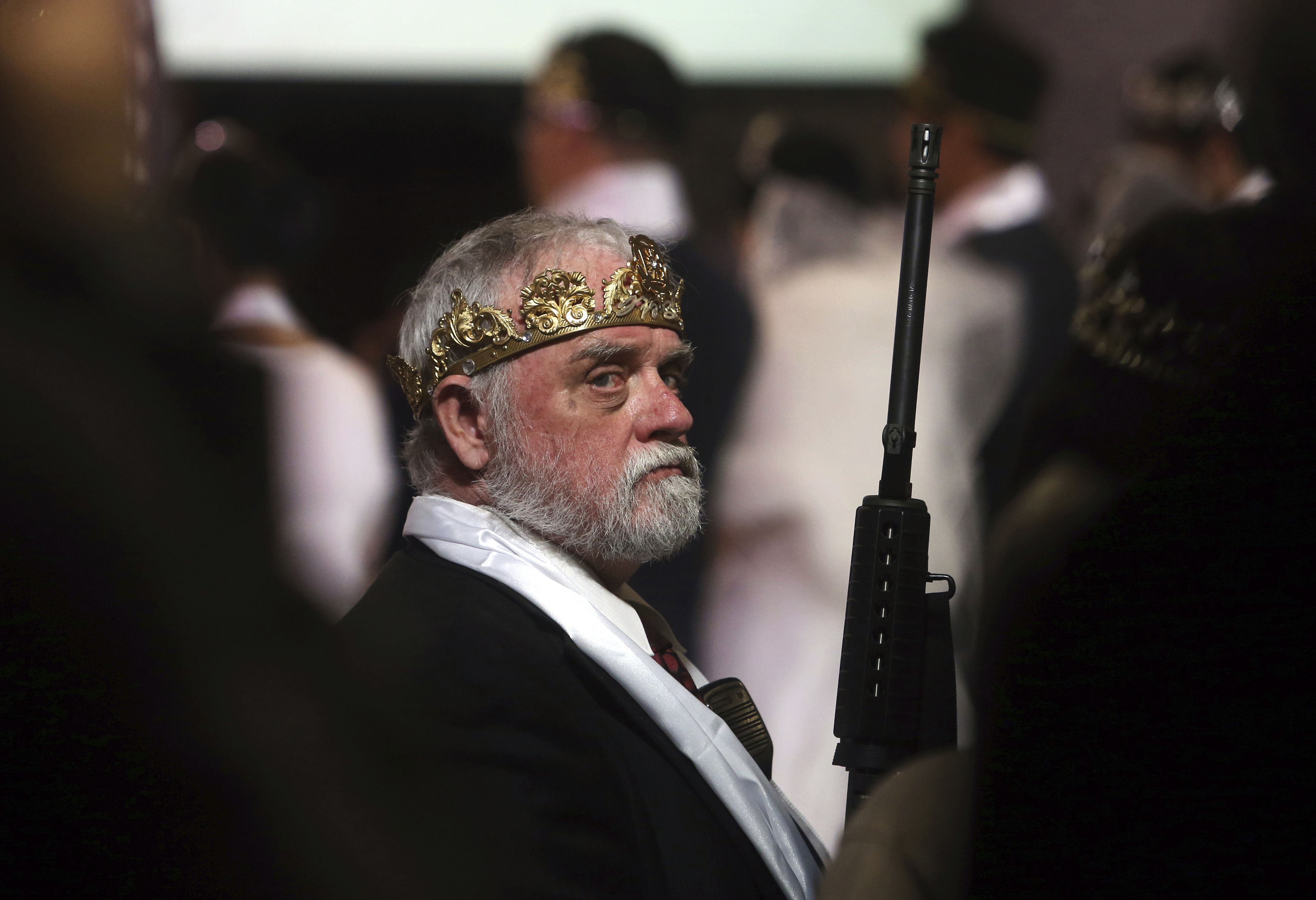 Man wears crown and holds rifle
