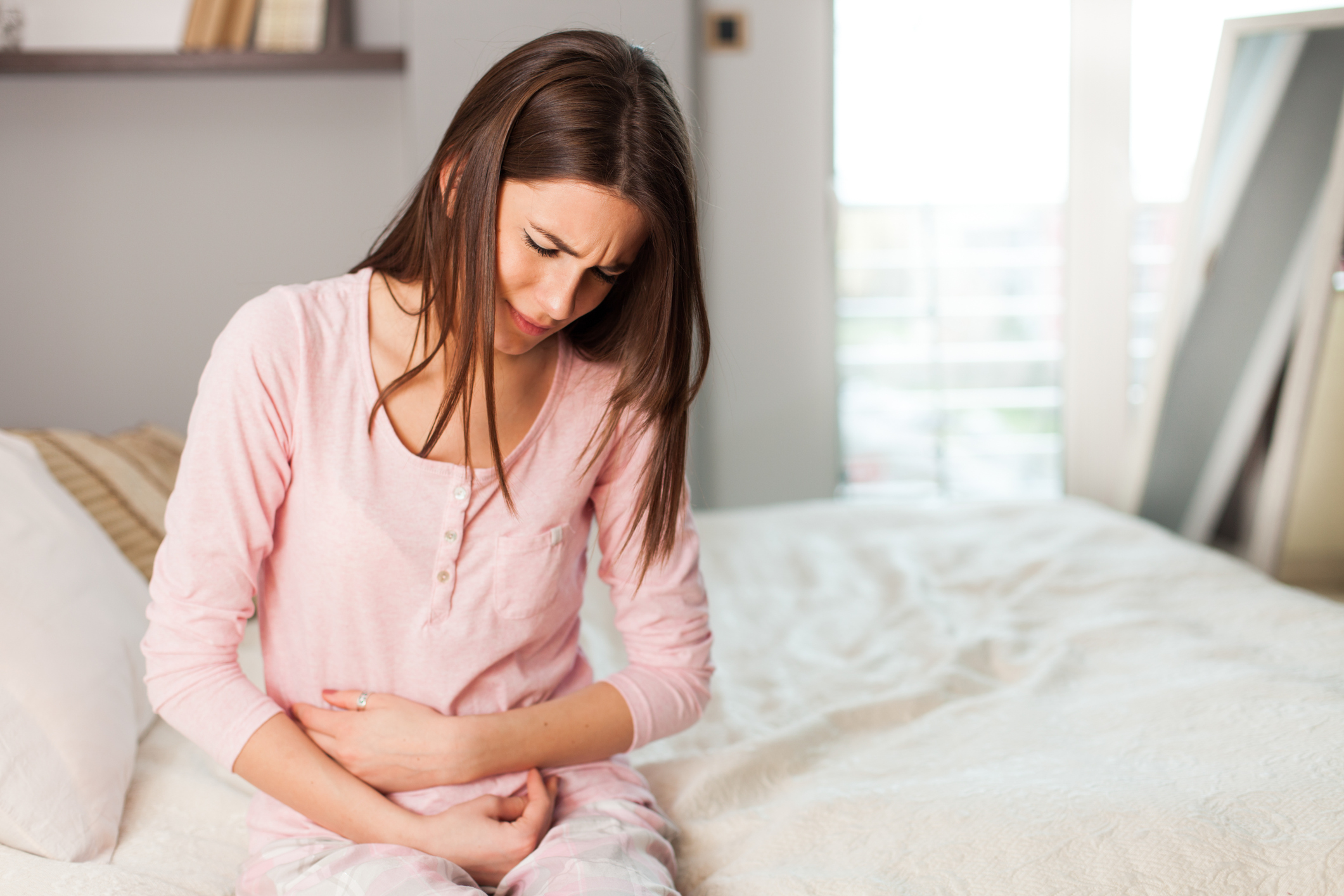 Young woman with a stomach ache in the bedroom, sitting holding her abdomen