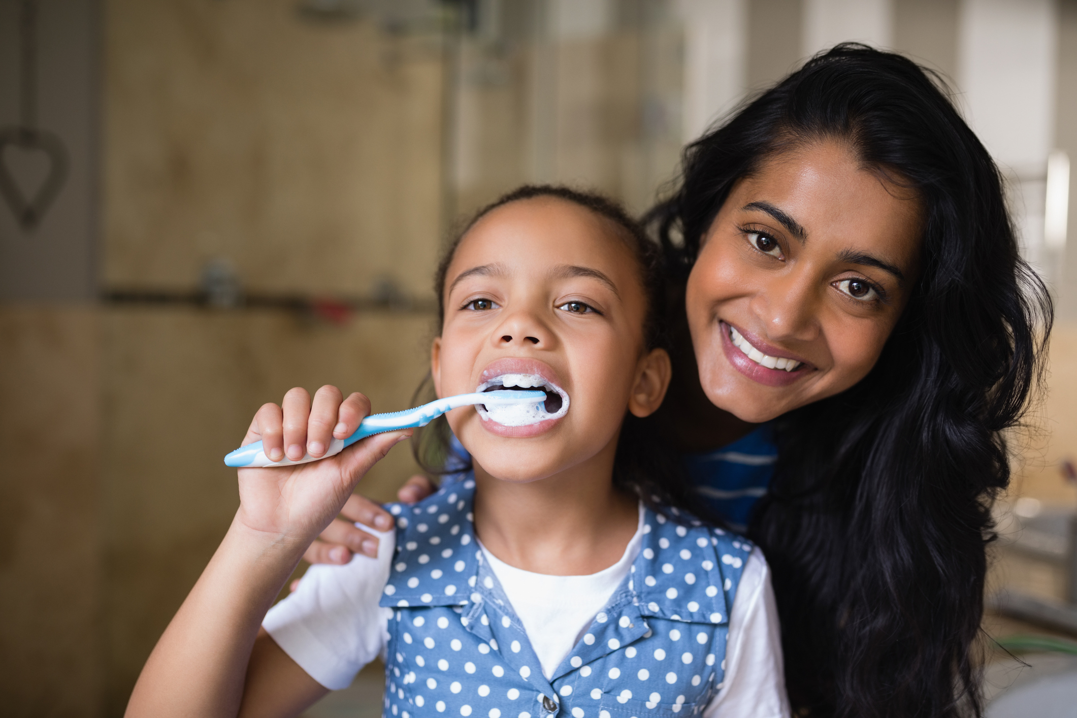 Close up of girl brushing teeth with mother in bathroom