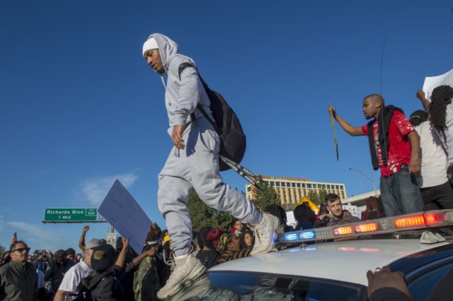 A protester walks across the top of a police car  (Renee C Byer/The Sacramento Bee via AP)