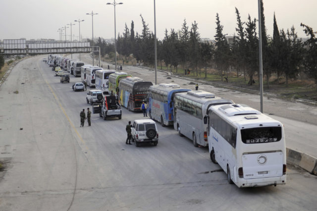 Syrian government forces oversee the evacuation by buses of rebel fighters and their families at a checkpoint in eastern Ghouta (SANA via AP)