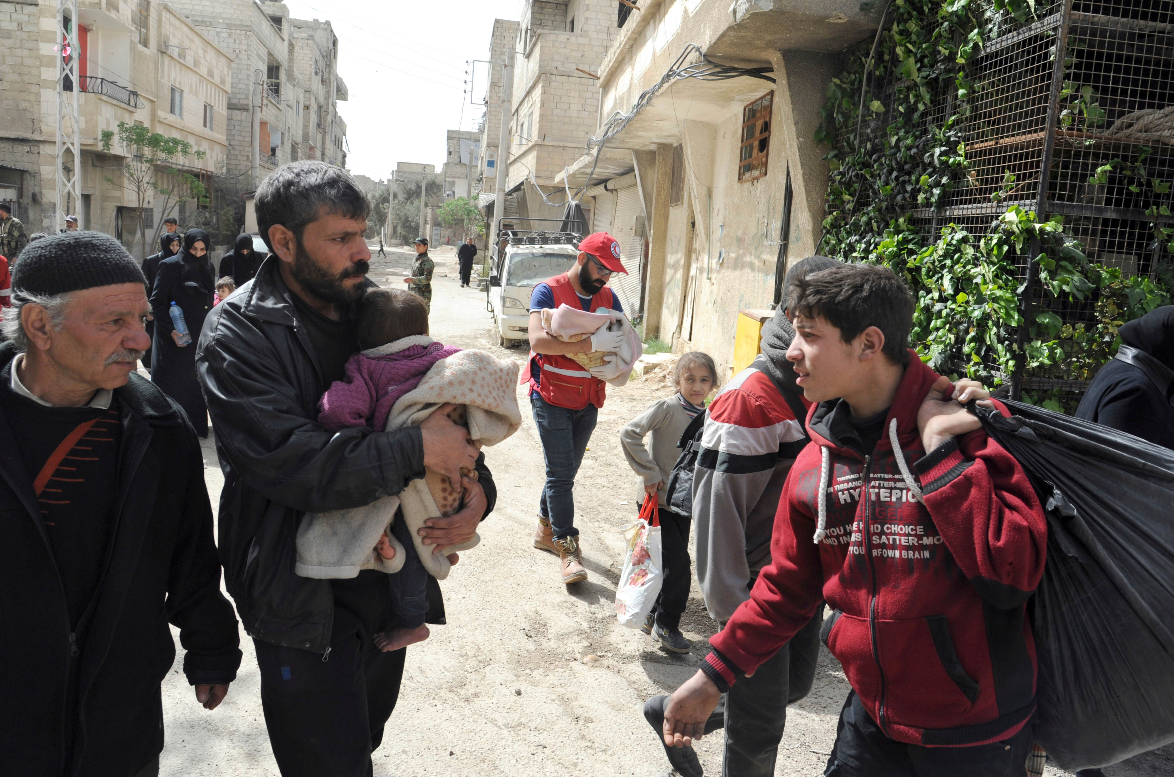 Civilians carrying their belongings as they left the rebel-held suburb of Douma (SANA via AP)