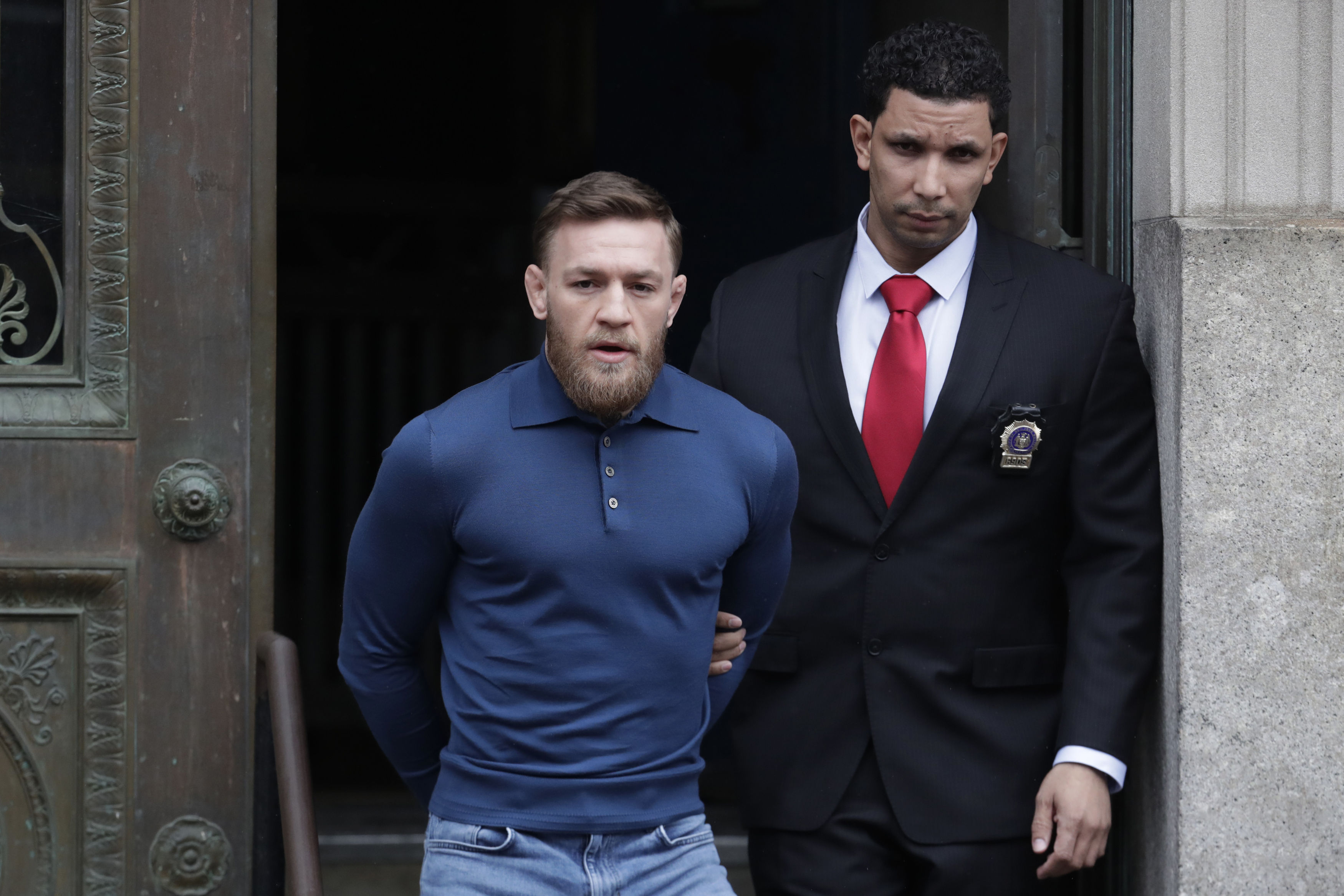 Conor McGregor, left, is led to an unmarked vehicle while leaving the 78th Precinct of the New York Police Department (AP Photo/Julio Cortez)