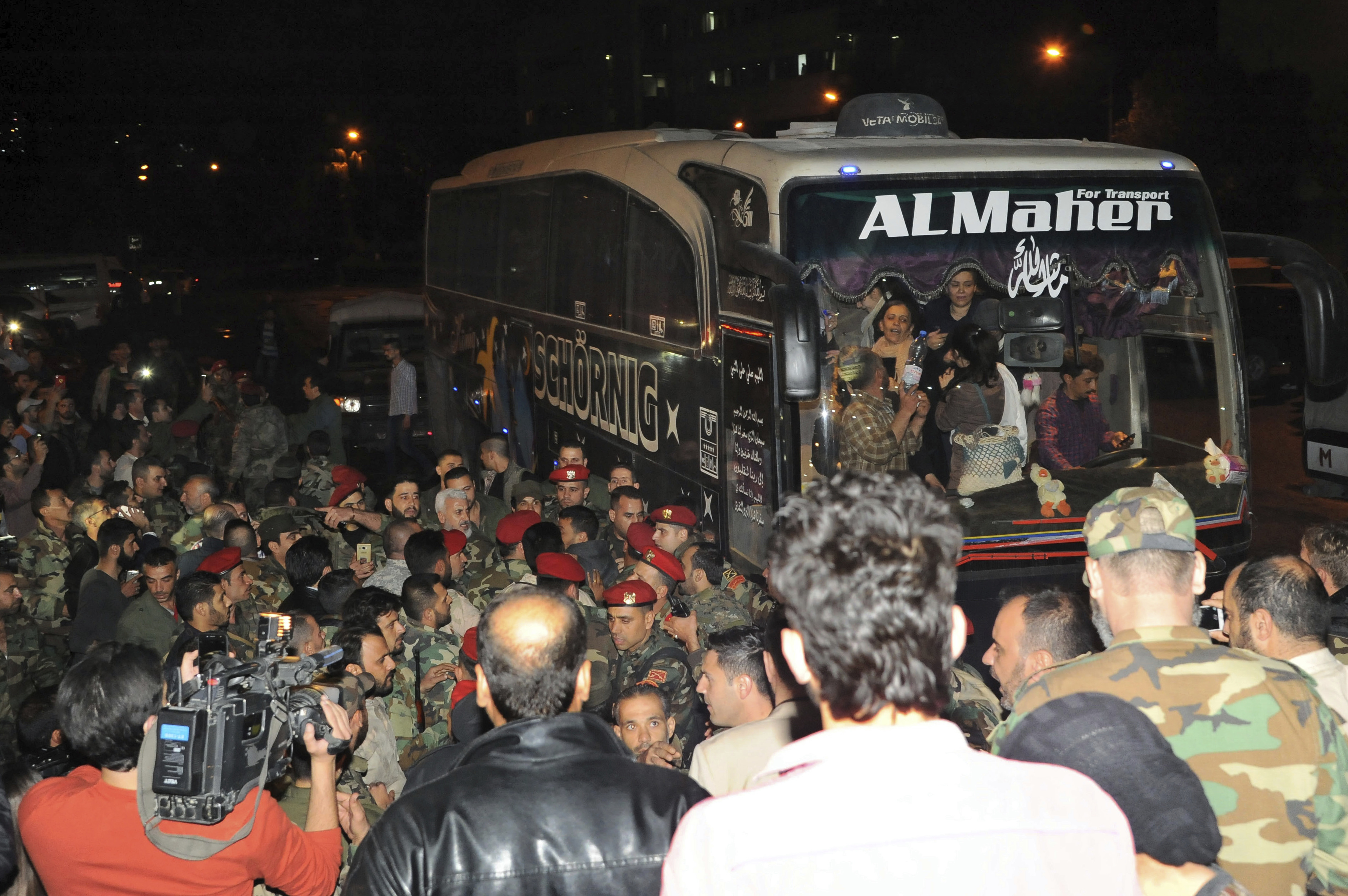 Soldiers and residents gather near a bus carrying civilians who  were released by the Army of Islam (SANA via AP)