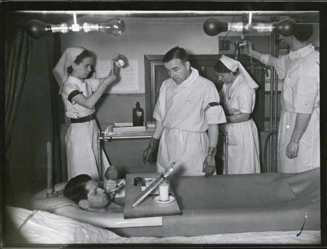 A burns patient enjoys a cigarette while in a saline bath while medical staff work in the background (Historic England Archive/PA)