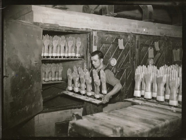 A man puts rubber gloves on moulds into an oven in a factory producing surgical gloves (Historic England Archive/PA)