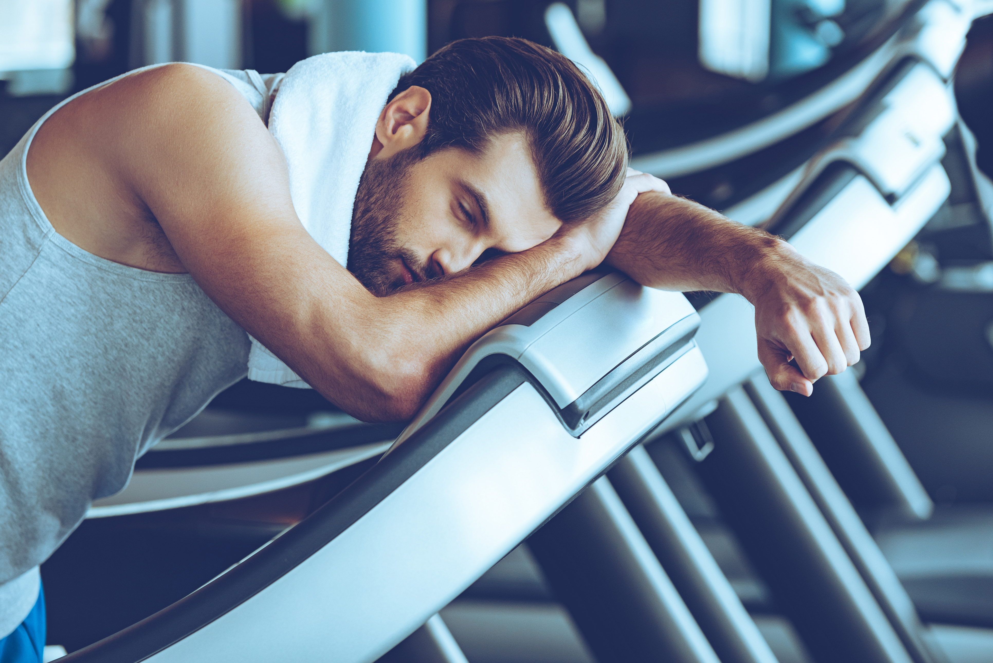 Side view of young man in sportswear looking exhausted while leaning on treadmill at gym