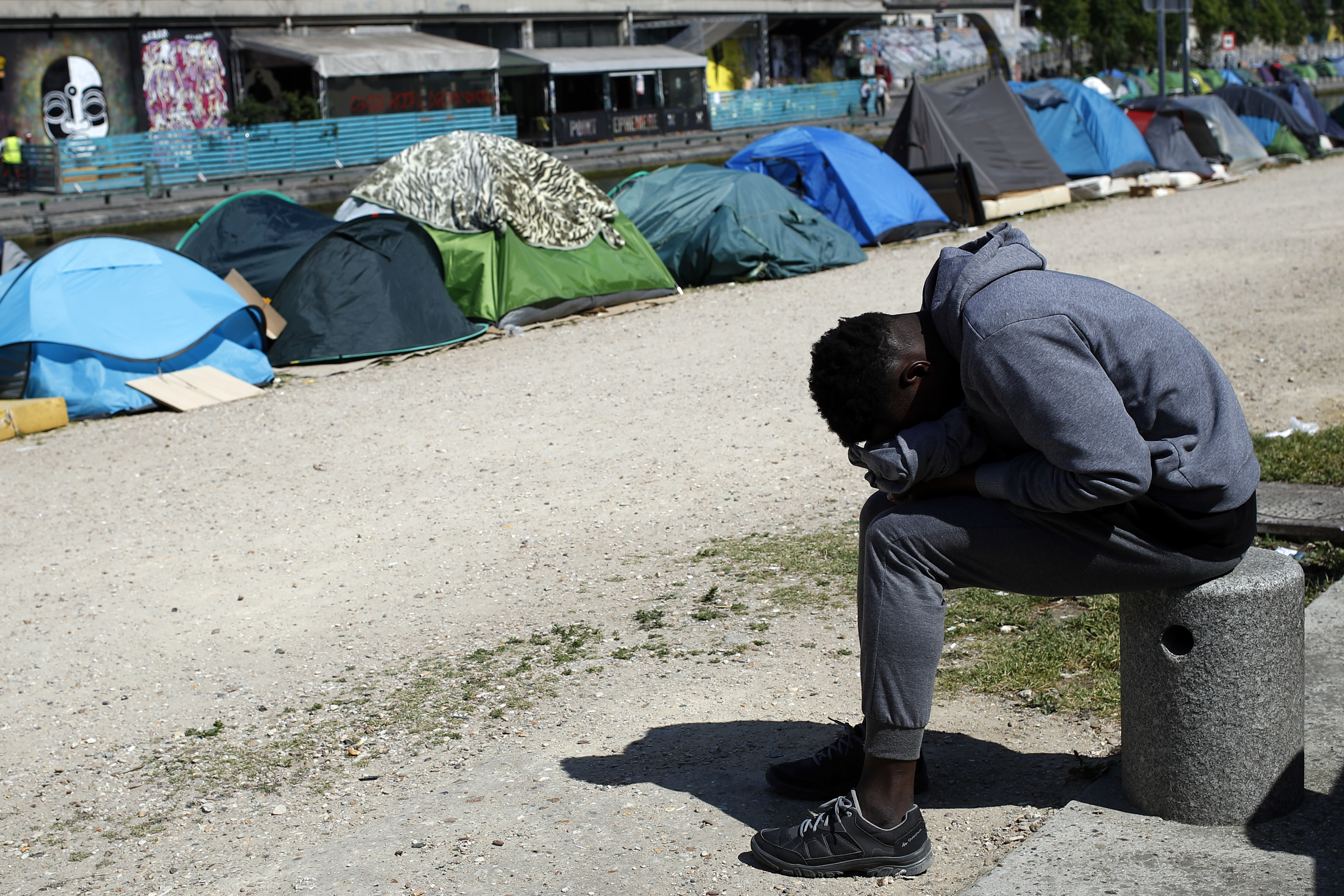 A migrant takes a nap near tents where asylum seekers live in a makeshift camp alongside the canal Saint-Martin (Francois Mori/AP)