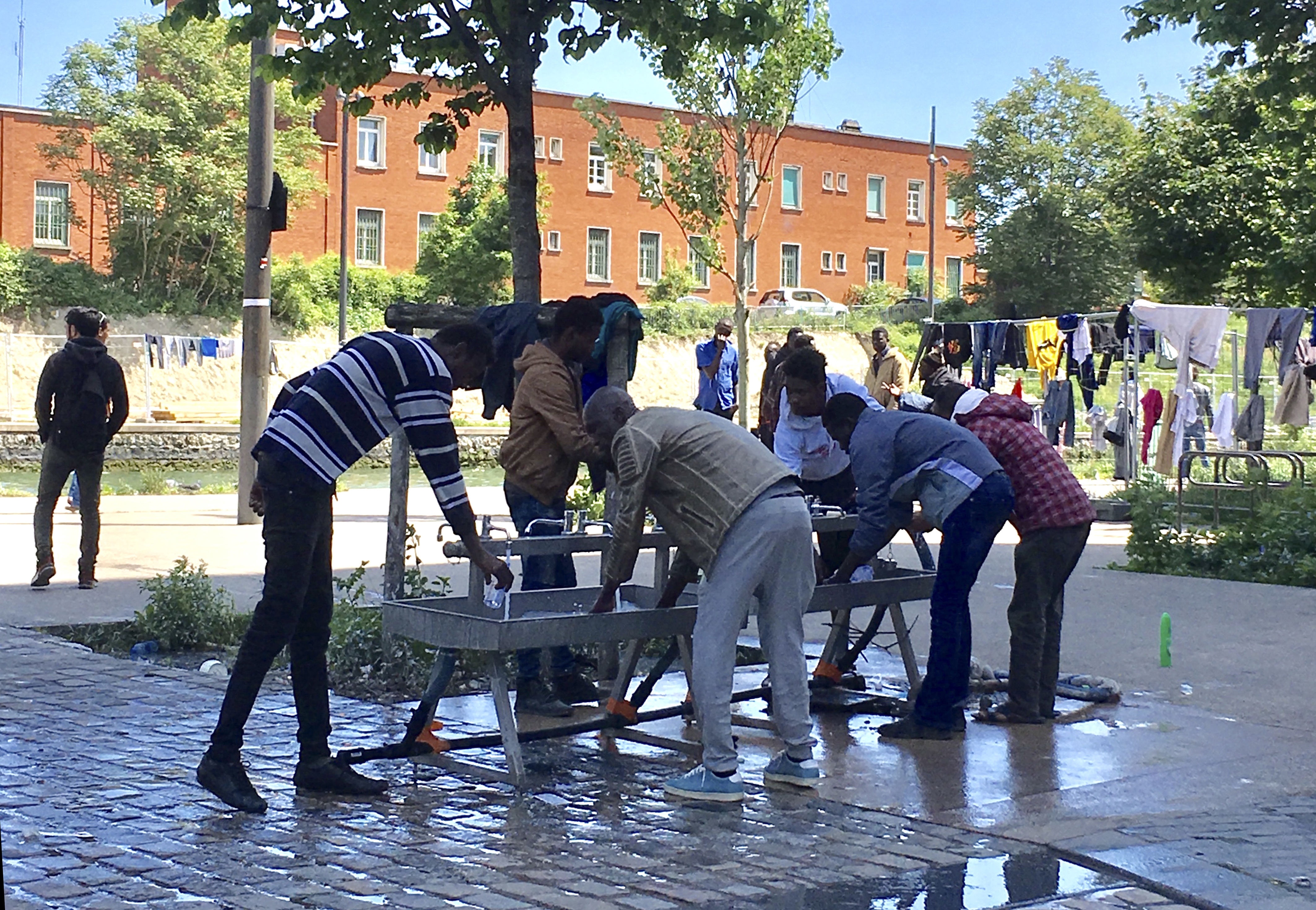 Migrants gather at the only water spigot at a migrant camp in Paris (Elaine Ganley/AP)